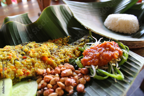 Traditional balinese food, Mujair Nyat-nyat, served on fresh banana leaf plating with various side dishes. Taken at Penglipuran Village, Bali, Indonesia photo