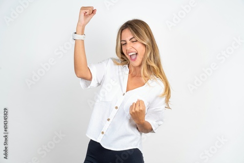 Profile photo of excited young blonde woman wearing white shirt over white studio background good mood raise fists screaming rejoicing overjoyed basketball sports fan supporter