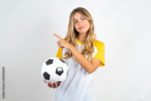 Young beautiful woman wearing football T-shirt over white background points to side on blank space demonstrates advertisement. People and promotion concept