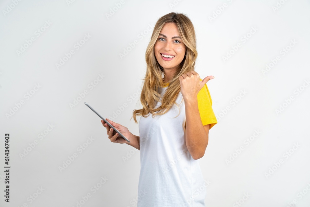 Young beautiful woman wearing football T-shirt over white background pointing empty space modern device Young beautiful woman wearing football T-shirt over white background pointing empty space modern device