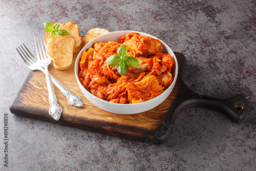 White fish stew with carrots and onions in spicy tomato sauce served with toast close-up on a wooden board on the table. horizontal photo