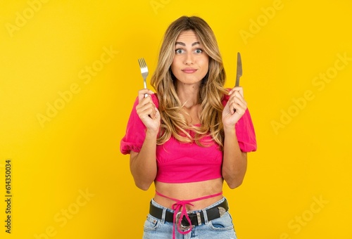 Fotografiet hungry young blonde woman wearing pink crop top over yellow studio background ho