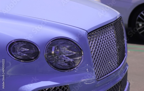 Unbranded SUV, sleek car closeup background image. Glistening newly cleaned car in the sunlight, blue paint scheme. Chrome grill and elegant headlights of car. Wallpaper of modern elegant luxury car.
