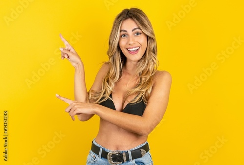 young beautiful blonde woman wearing bikini over yellow studio background points at copy space indicates for advertising gives right direction