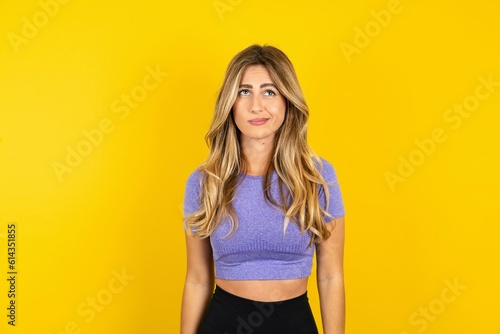 Displeased Young beautiful blonde woman wearing sportswear over yellow studio background frowns face feels unhappy has some problems. Negative emotions and feelings concept