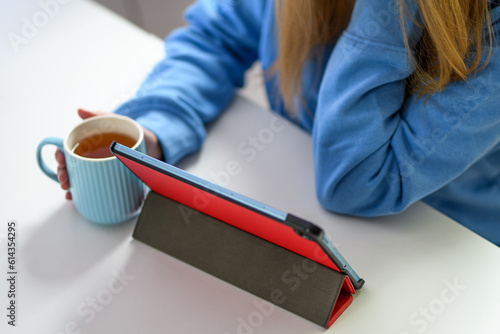Młoda kobieta korzysta z tabletu trzymając w ręce kubek herbaty 