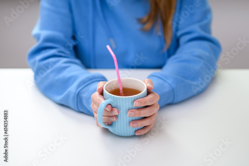 Picie ciepłego napoju czarnej herbaty z kubka przez plastikową słomkę