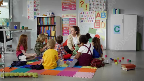 Obraz children sitting on floor while caring teacher explains lesson using toy in kindergarten