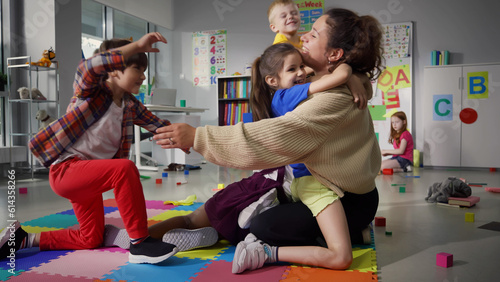 Fotografie Cheerful smiling teacher and happy diverse schoolchildren hugging in playroom of