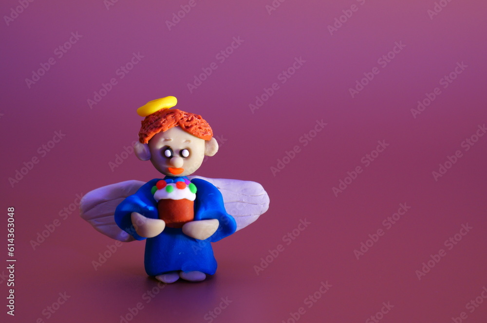 A little angel made of plasticine with a toy Easter. Bright colored background. A little angel made of plasticine with a toy Easter. Bright colored background.