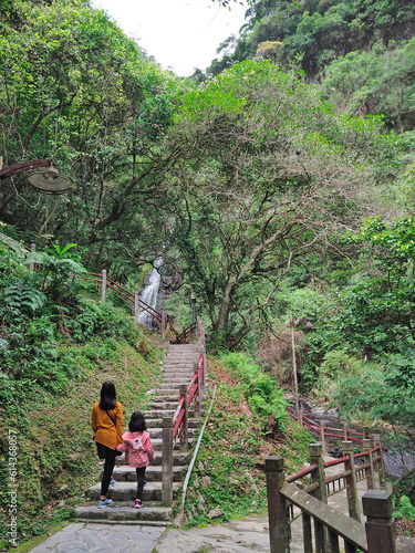 A woman and a little girl walking in the forest with a waterfall in the distance, at the Wufengqi Scenic Area in Jiaoxi, Yilan, Taiwan.