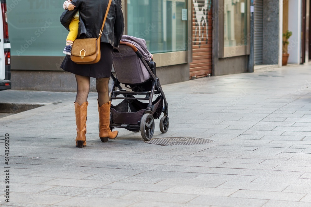 Woman with a baby in her arms and a baby carrier walking down a shopping street.