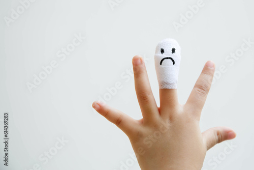 Injured middle finger of child with sad face on bandage