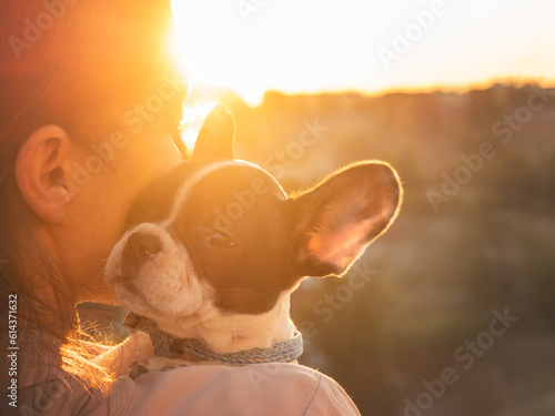 Cute puppy lies on a woman's shoulder. Clear, sunny day. Close-up, outdoors. Day light. Concept of care, education, obedience training and raising pets