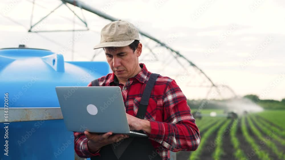 Agriculture.Farmer engineer is work with laptop in field.Automatic irrigation system for organic products on farm.Work engineer adjusts operation of irrigation system on farm.Agriculture food concept Agriculture.Farmer engineer is work with laptop in field.Automatic irrigation system for organic products on farm.Work engineer adjusts operation of irrigation system on farm.Agriculture food concept