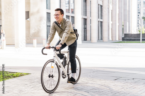 Fototapeta Naklejka Na Ścianę i Meble -  The guy with the business bag uses environmentally friendly transport. A young man riding a bicycle in formal clothes came to work in the office.
