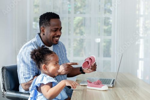 happy african father and little daughter Wearing a blue shirt using a laptop, shopping online, pink shoes happily.