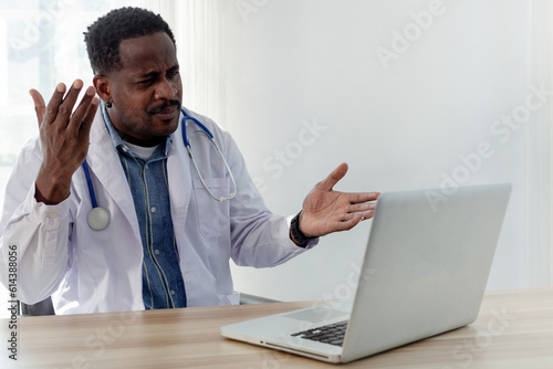 Medical concepts. An American male doctor uses an online meeting app on a laptop computer in a medical office.