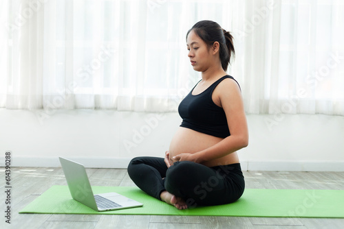 beautiful asian pregnant woman Practicing yoga with online classes on my laptop at home. fitness concept and health care