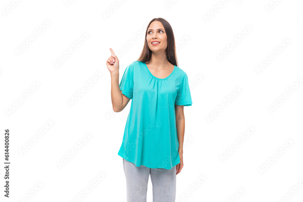 young brunette european lady with straight hair dressed in a blue t-shirt demonstrates with a hand gesture against a wall with advertising space young brunette european lady with straight hair dressed in a blue t-shirt demonstrates with a hand gesture against a wall with advertising space