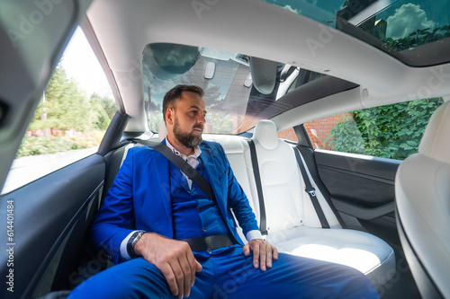 A caucasian man in a blue suit sits in the back seat of a car. Business class passenger. 