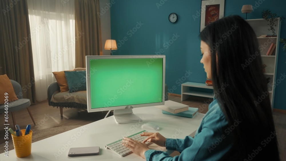 A young Asian woman works at a computer with a green screen close up. A longhaired brunette woman sits at a living room table. Side view. Advertising area, workspace mock up. A young Asian woman works at a computer with a green screen close up. A longhaired brunette woman sits at a living room table. Side view. Advertising area, workspace mock up.