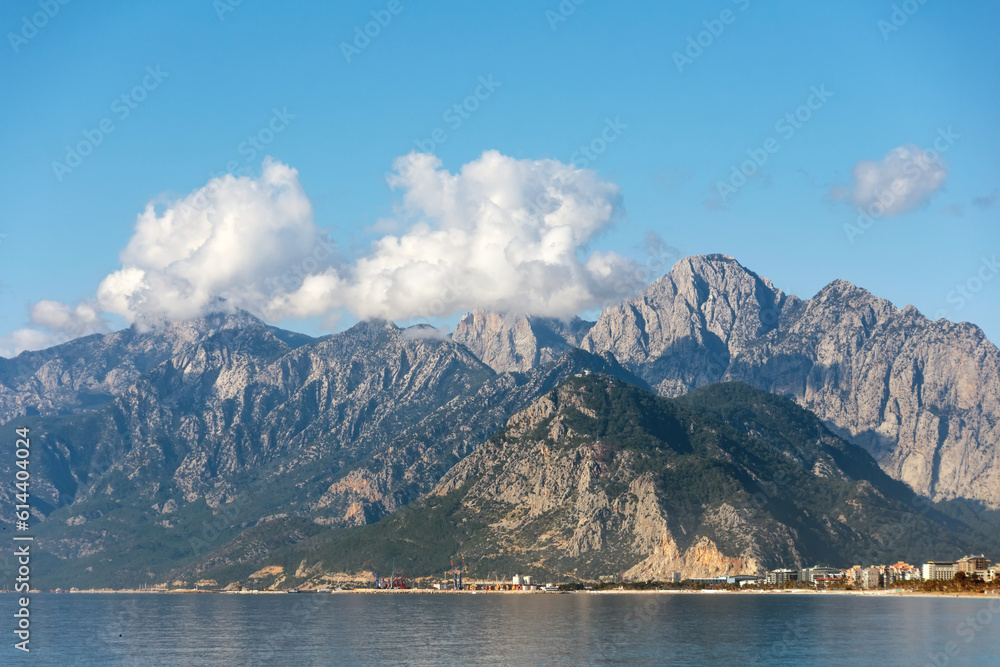 Amazing landscape on rocky mountains with a ship in the sea in the distance and cumulus clouds.