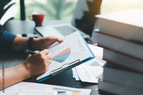 A young female of banking manger using calculator, computer laptop, paper worksheet to analyze data information. She is a professional financial of banking and calculating payment of currency exchange