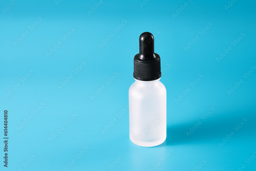 A glass bottle with a pipette containing a cosmetic product. Blue background. Copy space.