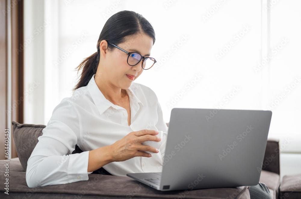 asian mature woman working on laptop in living room at home office. asian professor using computer remote teaching , virtual training, e-learning, watching online education webinar at home asian mature woman working on laptop in living room at home office. asian professor using computer remote teaching , virtual training, e-learning, watching online education webinar at home