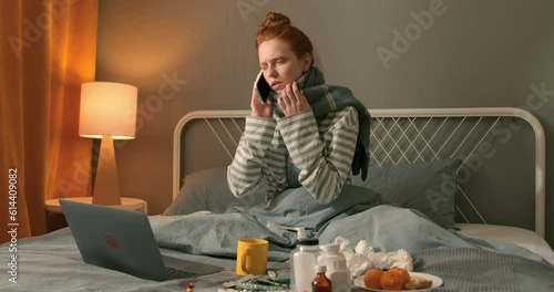 weak pale unwell red-haired woman making phone call, calling ambulance, consulting with doctor while sitting on bed, looking for informtion from laptop how treat illness Slow motion conversation photo