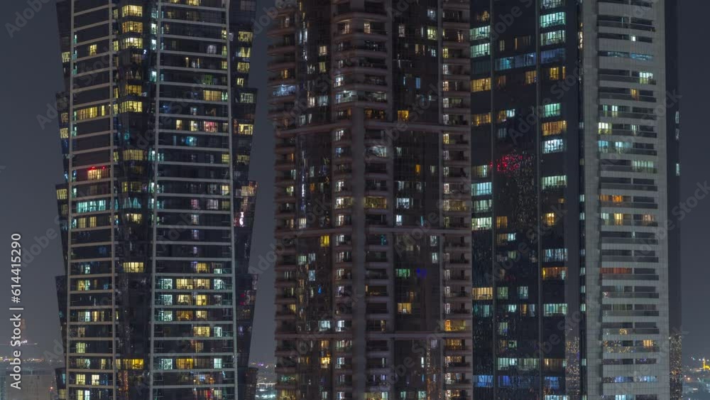 Tall blocks of flats with glowing windows located in residential district of city aerial timelapse. Evening light in rooms in high-rise towers and skyscrapers