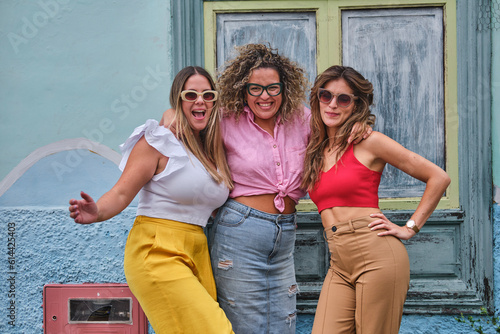 three girl friends in their 30s posing amusingly in front of an old house with blue door and window