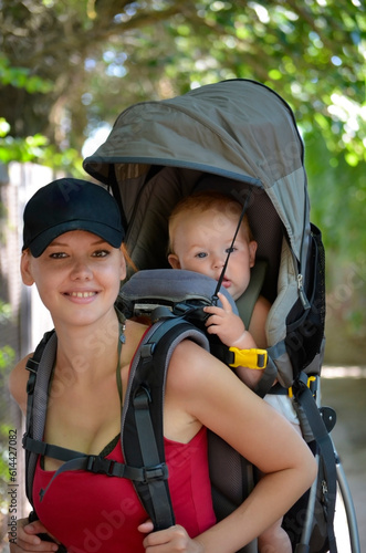 Happy young mother with a small child in a carrying bag on her back. Hiking with young children. Close-up portrait.