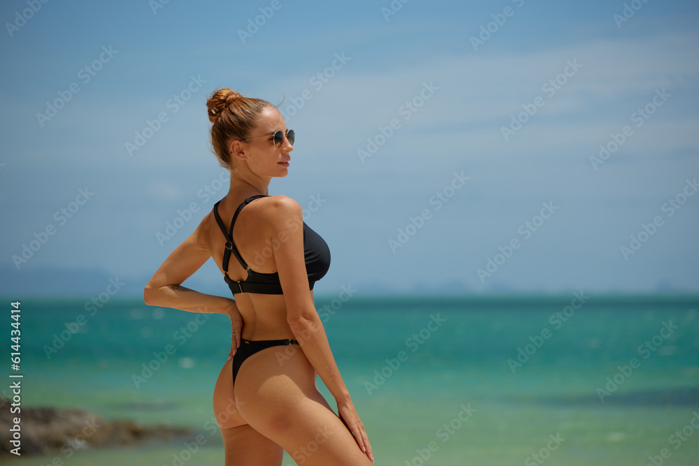Beautiful young woman in black swimsuit and sunglasses on the beach