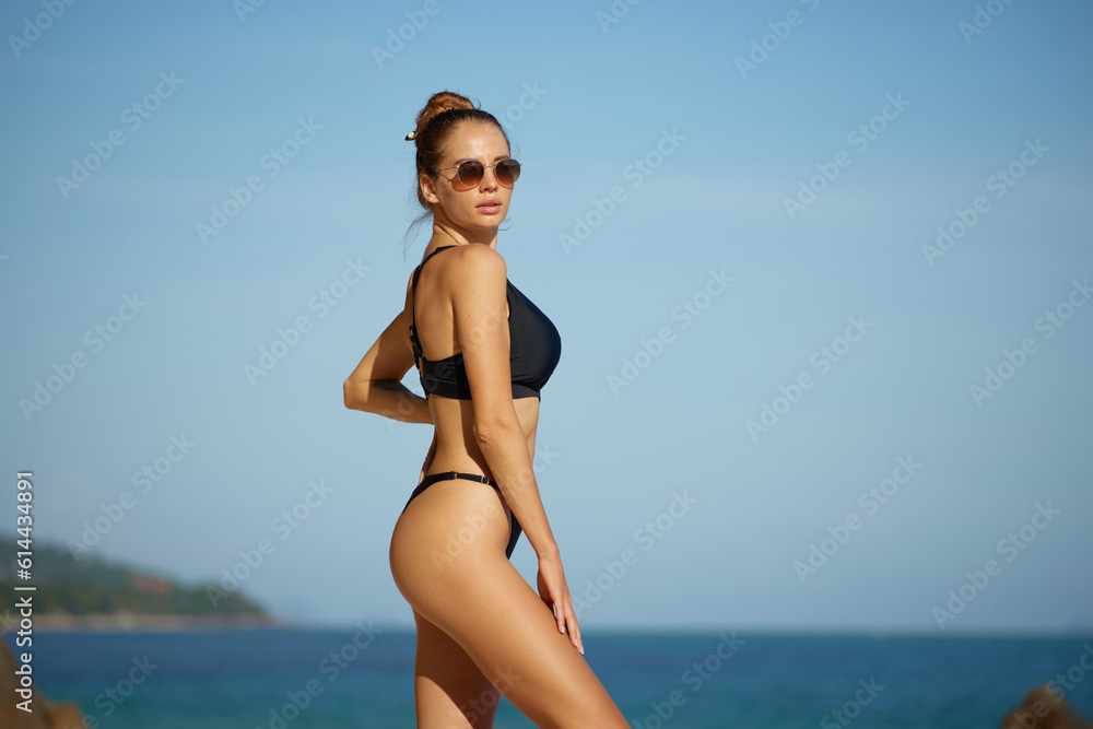 Beautiful young woman in black swimsuit and sunglasses on the beach