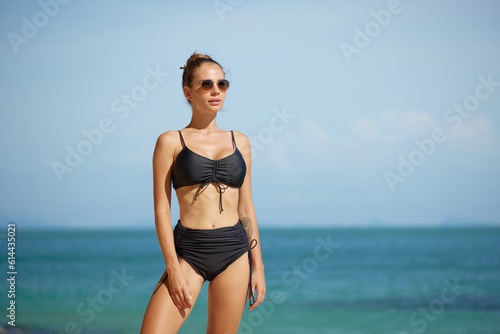 Beautiful young woman in black swimsuit and sunglasses on the beach
