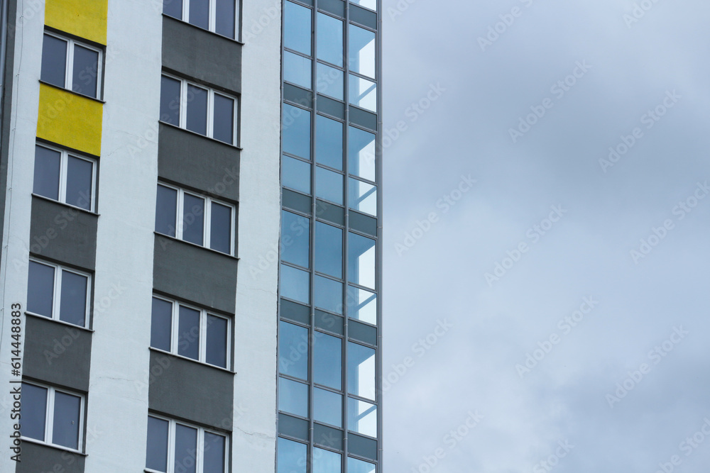 Windows and glazed balconies of an apartment building against a cloudy sky.