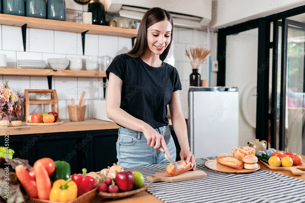 Woman slicing bread with knife on wooden cutting board and prepa Woman slicing bread with knife on wooden cutting board and prepa