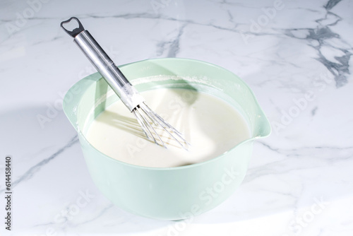 Liquid dough in an iron bowl with a whisk. Preparing dough for a sweet pie , stir the dough with a black whisk in a deep transparent bowl 