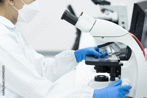 Women scientist looking to microscope eyepiece in clinical laboratory.Young scientist doing some research.Medical technician analysis blood slide on exam plate microscopic at laboratory department.