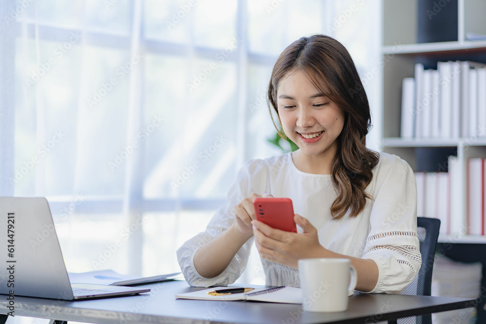 Smiling Asian woman talking on the phone with a customer Young positive female accountant using smartphone talking to team at her desk relaxing with mobile application Smiling Asian woman talking on the phone with a customer Young positive female accountant using smartphone talking to team at her desk relaxing with mobile application