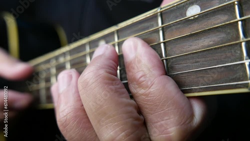 Man strumming a guitar. Musician playing guitar in a music studio. Person playing an acoustic guitar. Acoustic guitar close-up shot. Guitar neck, guitar arm. Guitar strings. Chords. Guitar fretboard.  photo