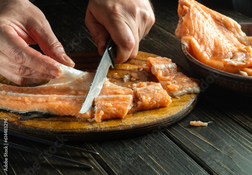 The chef cuts salmon raw fish on a kitchen board. Cooking a national fish dish with the hands of a cook on the kitchen table in a restaurant