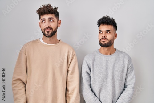 Young homosexual couple standing over white background smiling looking to the side and staring away thinking.