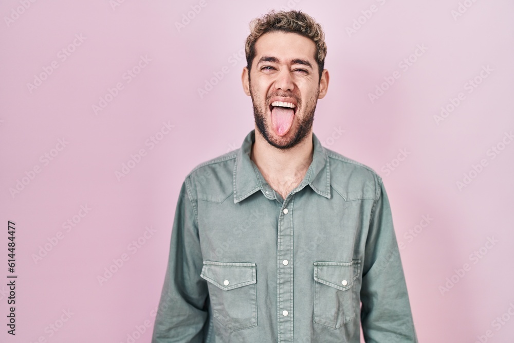 Fototapeta premium Hispanic man with beard standing over pink background sticking tongue out happy with funny expression. emotion concept.
