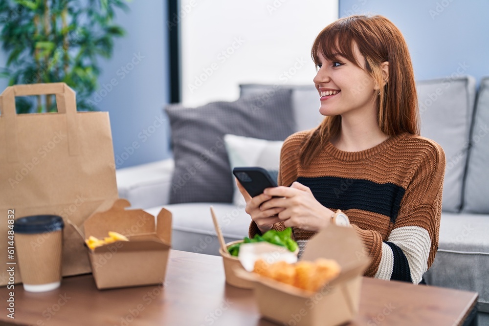 Young woman using smartphone eating take away food at home Young woman using smartphone eating take away food at home