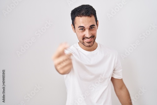 Handsome hispanic man standing over white background beckoning come here gesture with hand inviting welcoming happy and smiling