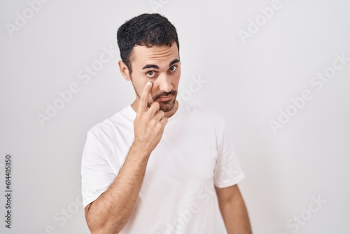 Handsome hispanic man standing over white background pointing to the eye watching you gesture, suspicious expression
