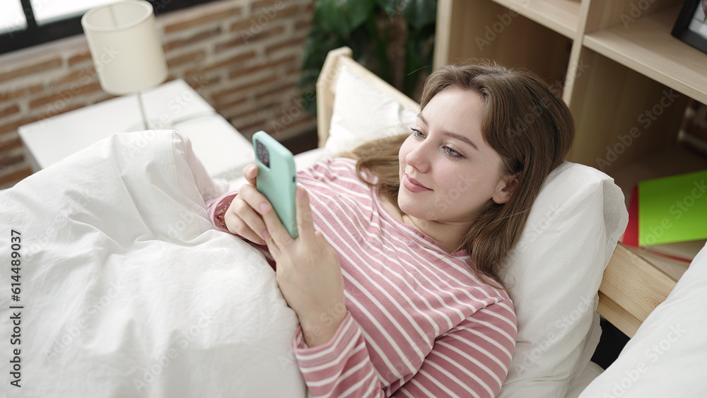 Young blonde woman using smartphone lying on bed at bedroom Young blonde woman using smartphone lying on bed at bedroom